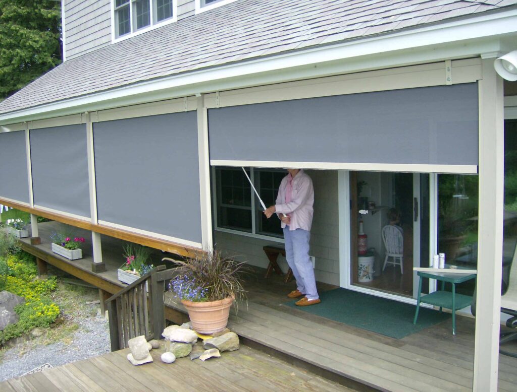 An outdoor porch with exterior solar screens and a person manually operating them to go up and down