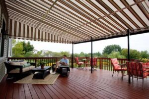 Deck canopy in red stripe with deck furniture and a person.