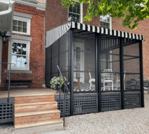 Black and white striped deck canopy with screen panels on historic brick house.
