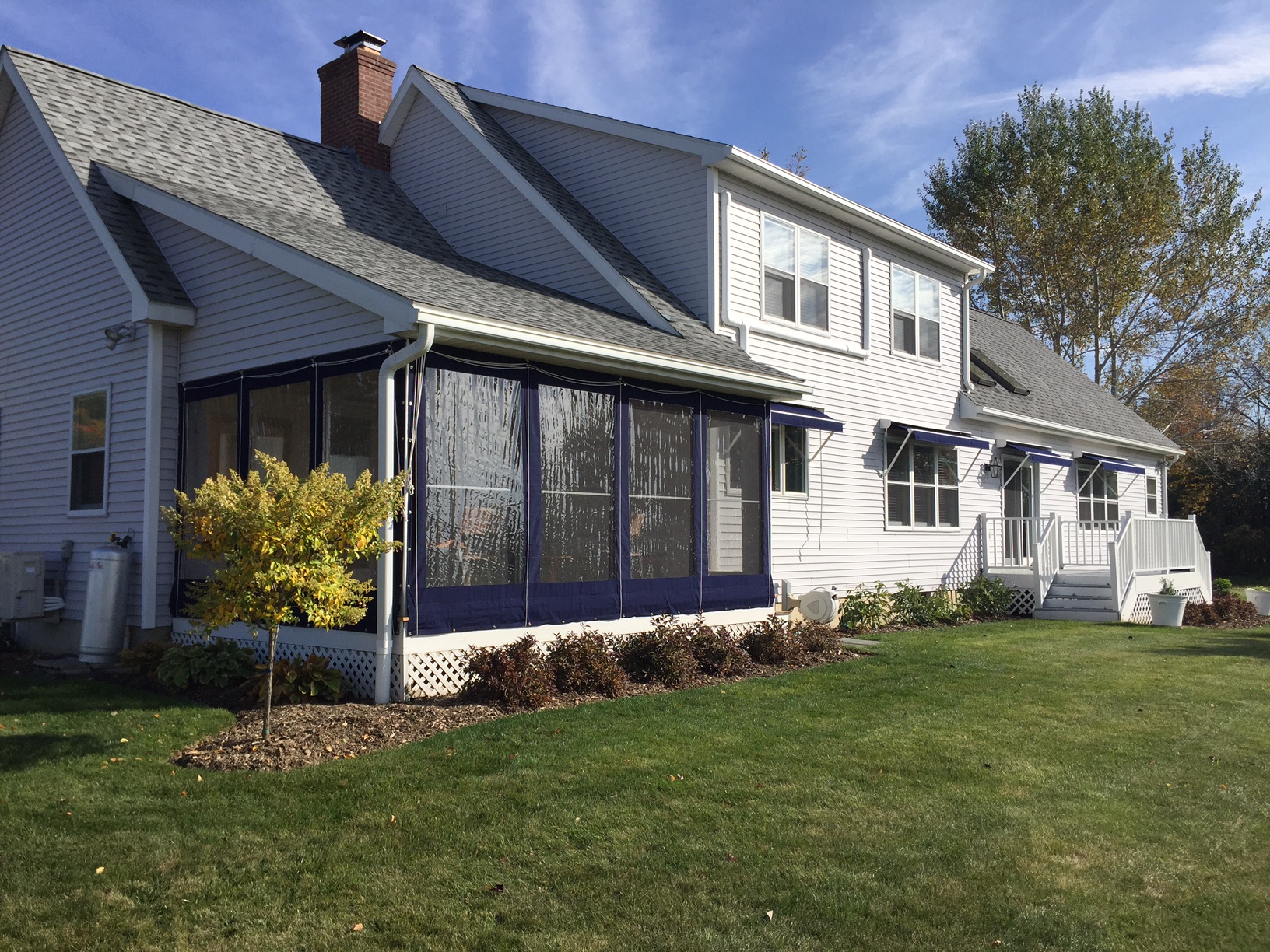 Cape style house with gray siding and blue window and porch curtains.